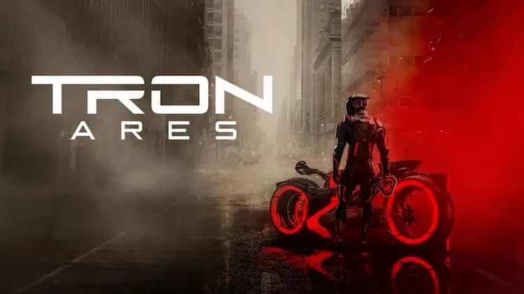 A promotional movie poster for "Tron: Ares" featuring a person in a black and red futuristic high-tech suit standing next to a sleek, glowing red Light Cycle on a rain-slicked city street. The character is viewed from behind, looking toward a foggy urban background. The "Tron Ares" logo is prominently displayed in white text on the left.