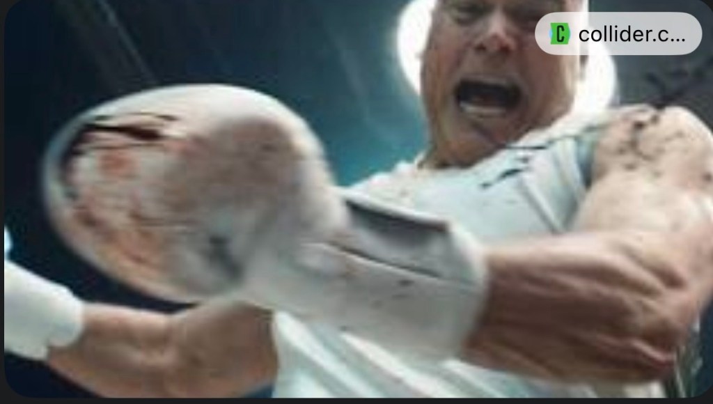 A dramatic, low-angle shot of Wilson Fisk (Vincent D’Onofrio) in a boxing ring. He wears white boxing trunks and is illuminated by harsh red arena lights. Behind him, shards of glass catch the light, and the atmosphere is heavy with tension and smoke.