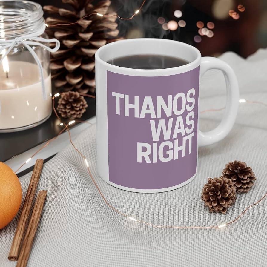A white ceramic mug with a square purple graphic printed on the side that reads 'THANOS WAS RIGHT' in bold white capital letters. The mug is sitting on a grey fabric surface next to two small pinecones, a candle in a glass jar, and a few cinnamon sticks.