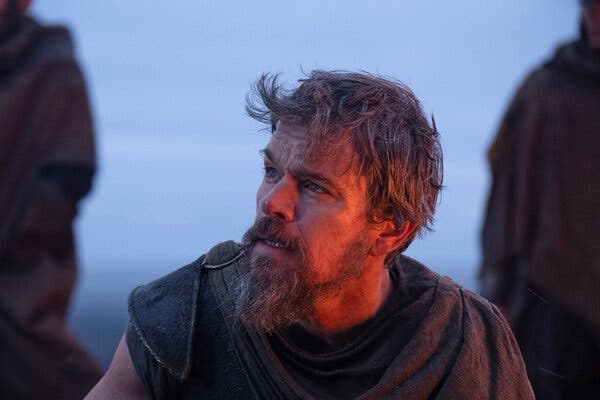 Matt Damon as a weathered, bearded Odysseus wearing a rough-hewn tunic in a dramatic, dimly lit scene from Christopher Nolan's The Odyssey.