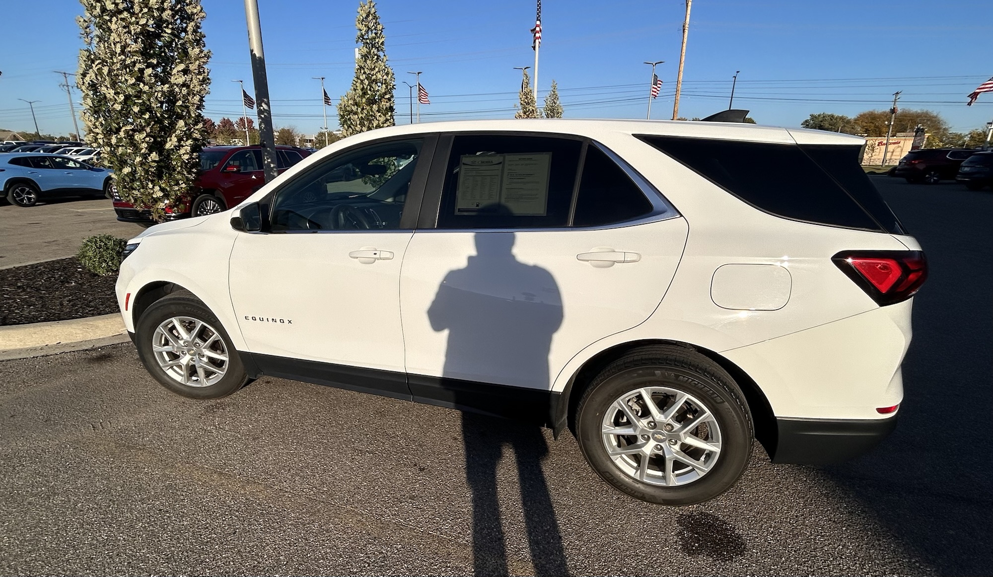 A full-body, passenger-side profile of a white Chevrolet Equinox SUV in a sunny outdoor setting on a paved surface